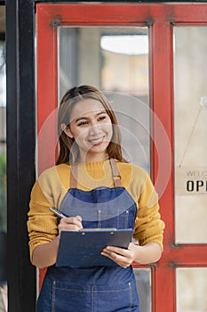 Attractive Asian female business owner in apron with open door sign vertical image