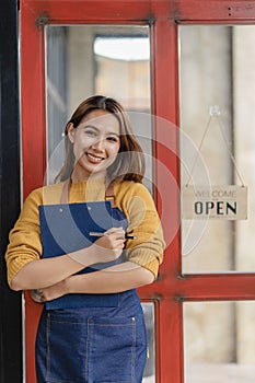 Attractive Asian female business owner in apron with open door sign vertical image