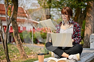 Attractive Asian female college student using laptop on a bench in campus park