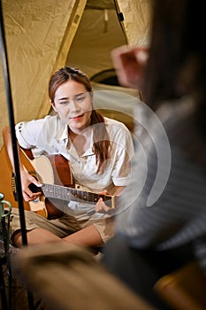 Attractive Asian female enjoy playing guitar and singing with her friends at night in the campground