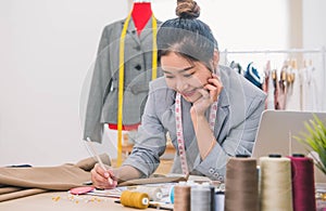 Attractive Asian female fashion designer  working in home office workshop. Stylish fashionista woman creating new cloth design