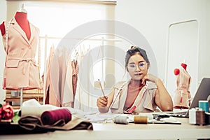 Attractive Asian female fashion designer working in home office workshop. Stylish fashionista woman creating new cloth design