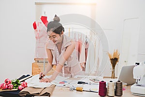 Attractive Asian female fashion designer working in home office workshop. Stylish fashionista woman creating new cloth design