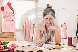 Attractive Asian female fashion designer working in home office workshop. Stylish fashionista woman creating new cloth design