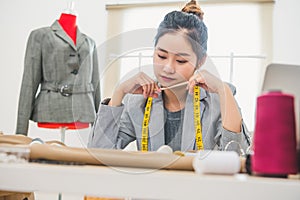 Attractive Asian female fashion designer working in home office workshop. Stylish fashionista woman creating new cloth design