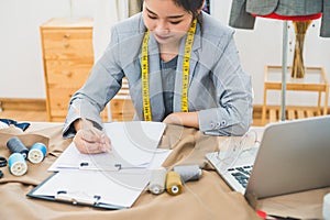 Attractive Asian female fashion designer working in home office workshop. Stylish fashionista woman creating new cloth design