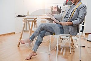 Attractive Asian female fashion designer working in home office workshop. Stylish fashionista woman creating new cloth design