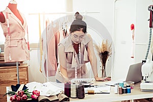 Attractive Asian female fashion designer working in home office workshop. Stylish fashionista woman creating new cloth design