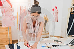 Attractive Asian female fashion designer working in home office workshop. Stylish fashionista woman creating new cloth design