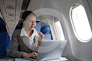 Attractive Asian female passenger on airplane sitting in comfortable seat using laptop and credit card, shopping using