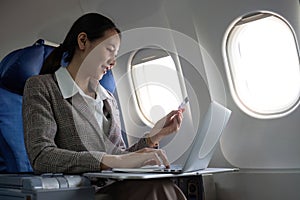 Attractive Asian female passenger on airplane sitting in comfortable seat using laptop and credit card, shopping using