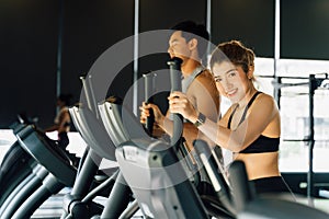 Attractive Asian fitness woman using elliptical trainer at the gym and looking at camera. Healthy and weight loss