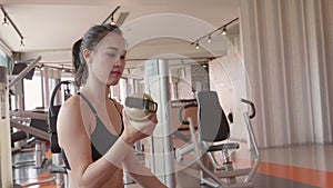 Attractive Asian girl drinking water from bottle in fitness sport gym. Close-up of young woman enjoying fresh water