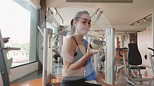 Attractive Asian girl drinking water from bottle in fitness sport gym. Close-up of young woman enjoying fresh water