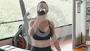 Attractive Asian girl drinking water from bottle in fitness sport gym. Close-up of young woman enjoying fresh water