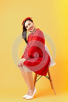 Attractive Asian girl sitting on modern chair isolated on orange background