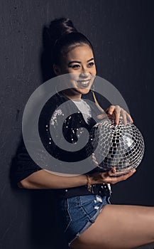 Attractive asian girl smiling and posing with disco ball in studio