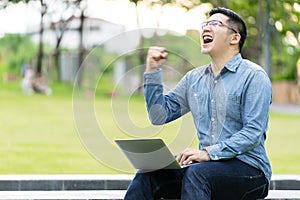 Attractive asian happy man gesture or raise hand excited screaming yes reading online good news or social network in laptop