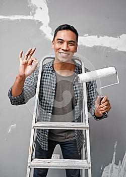 An attractive Asian man shows OK hand gesture while preparing to paint