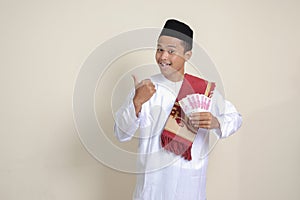 attractive Asian muslim man in white shirt showing one hundred thousand rupiah while pointing to the side. Financial