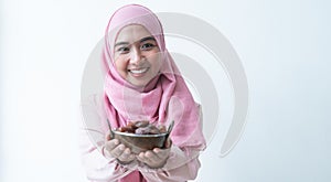 Attractive Asian 30s Muslim woman wearing traditional clothes with pink hijab head scarf, holding a bowl of dry dates fruit in han