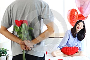 Attractive Asian woman being excited from her boyfriend surprise gift, man hiding beautiful red rose bouquet behind back, ready to