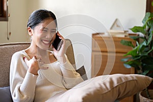 An attractive Asian woman enjoys talking with her friend on the phone while relaxing on a couch