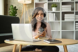 Attractive asian woman listening to music on headphone and reading book at home. People, leisure and lifestyle concept