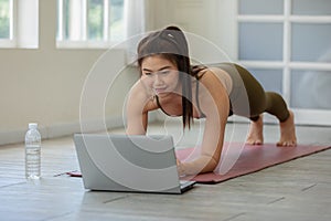 Attractive Asian woman looking laptop practice yoga plank online course at home