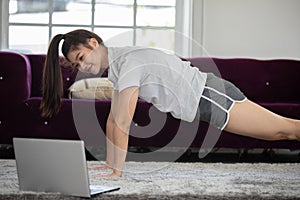 Attractive Asian woman looking laptop practice yoga plank online course at home