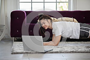 Attractive Asian woman looking laptop practice yoga plank online course at home