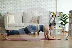 Attractive Asian woman looking laptop practice yoga plank online course at home to meditation comfortable and relax,Health care