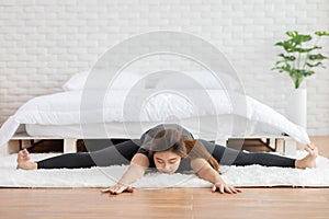 Attractive Asian woman practice yoga upavistha konasana or Seated angle pose to meditation in bedroom after wake up