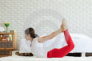 Attractive Asian woman practice yoga yoga bow or dhanurasana pose to meditation in bedroom after wake up in the morning