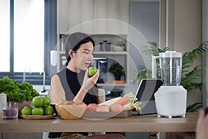Attractive asian woman searching recipes on digital tablet and preparing healthy smoothie in kitchen
