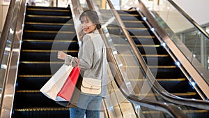 An attractive Asian woman with shopping bags is going up an escalator in a shopping mall