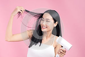 Attractive Asian woman usinf hair dryer on pink background