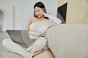 Attractive asian woman using laptop computer while sitting on a couch at home.