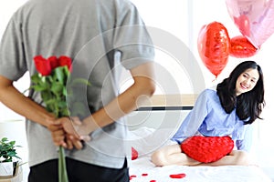 Attractive Asian woman being excited from her boyfriend surprise gift, man hiding beautiful red rose bouquet behind back, ready to