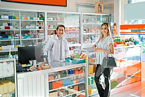 Attractive asian woman smiling at camera while male pharmacist working