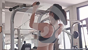 Attractive Asian young muscular girl in sportswear doing pull-ups exercise and chin up at fitness sport gym for strength workout