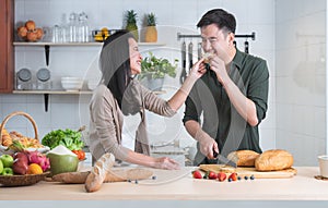 Attractive Asian young sweet couple cooking together in home kitchen. Beautiful woman smiling feeding her handsome man with bread