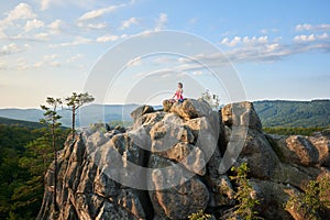 Attractive athletic barefooted girl sitting in lotus pose on lit by summer sun top of huge rock