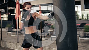 Attractive athletic female boxer in gloves kicking a punching bag. Workout outside. Female boxer training. Self defence