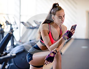 Attractive athletic girl in the sportswear uses the fitness app on your smartphones in the gym. Athlete enjoys her training.