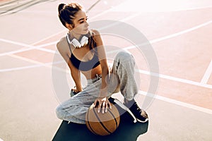 Attractive athletic young woman outdoor posing sitting on basketball court holding basketball