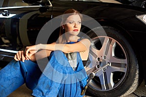 Attractive auto mechanic girl sits near wheel of black car