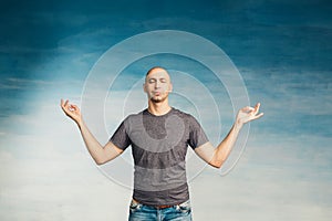Attractive bald man with closed eyes and a calm face on a blue background holds his hands in a meditation pose