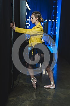 attractive ballerina in tutu and yellow leather jacket stretching