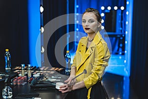 attractive ballerina in yellow leather jacket applying makeup